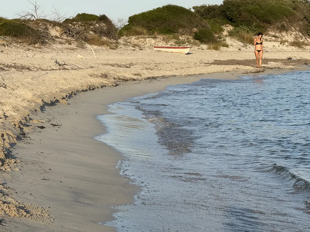 Spiaggia curva con acqua bassa, una persona in lontananza