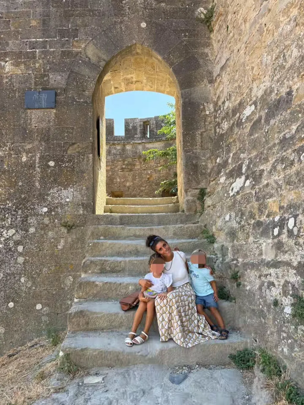 Sotto un arco, tre persone sedute su una scala di pietra, dietro il verde.