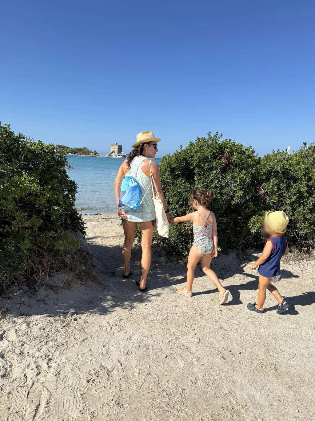 Una donna e due bambini scendono un sentiero sabbioso verso la spiaggia.