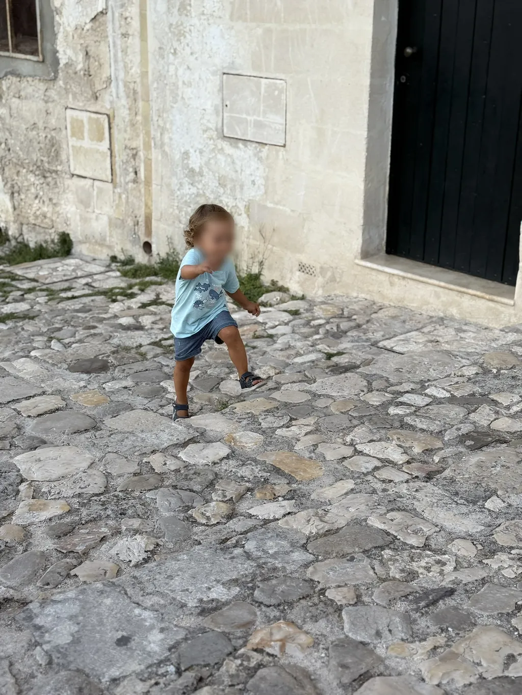 Un bambino corre sul selciato davanti a una porta scura.