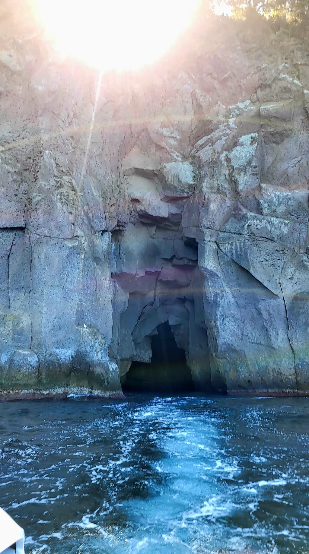 Una grotta nella parete di roccia, davanti l'acqua che spumeggia.