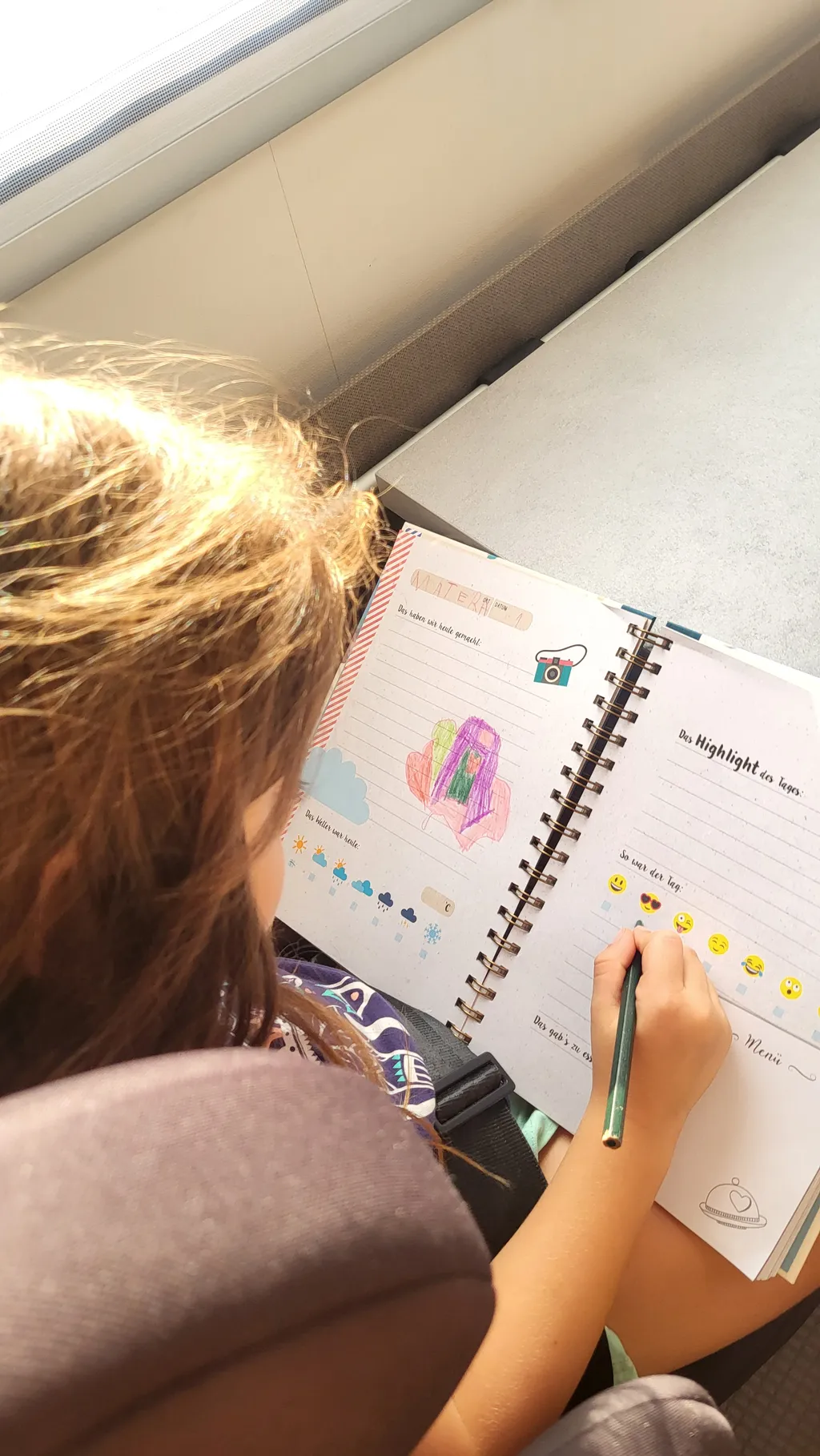 Un bambino, visto da dietro, scrive su un diario colorato.