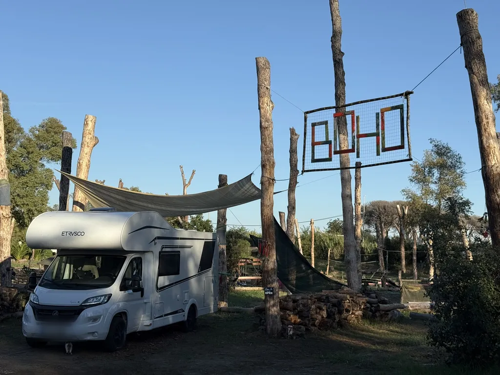 Un camper sotto alberi tagliati, accanto un canestro con la scritta BOHO.