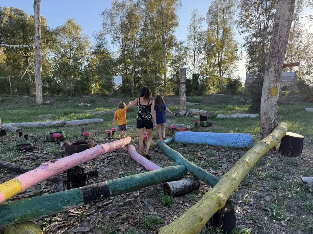 Una donna e due bambini in equilibrio su tronchi dipinti a colori.