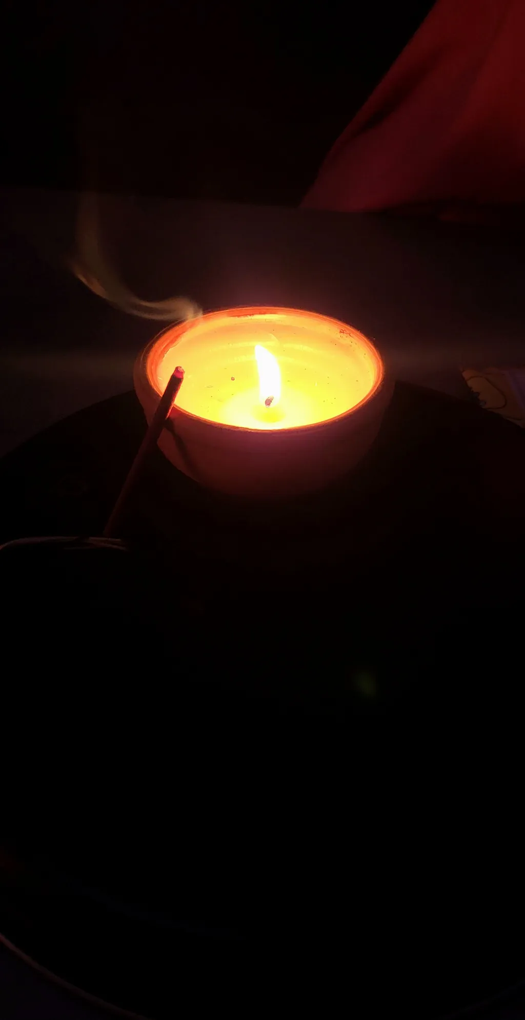Una candela accesa in un bicchiere, accanto un bastoncino d'incenso.