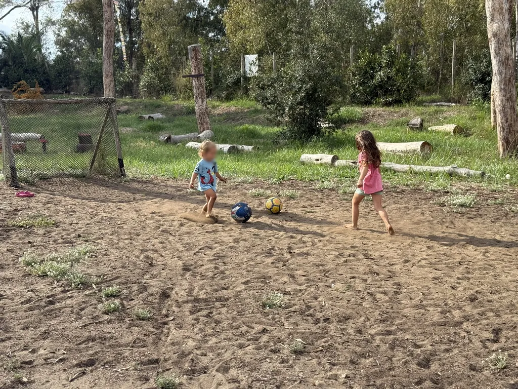 Due bambini giocano con due palloni su un terreno sabbioso.