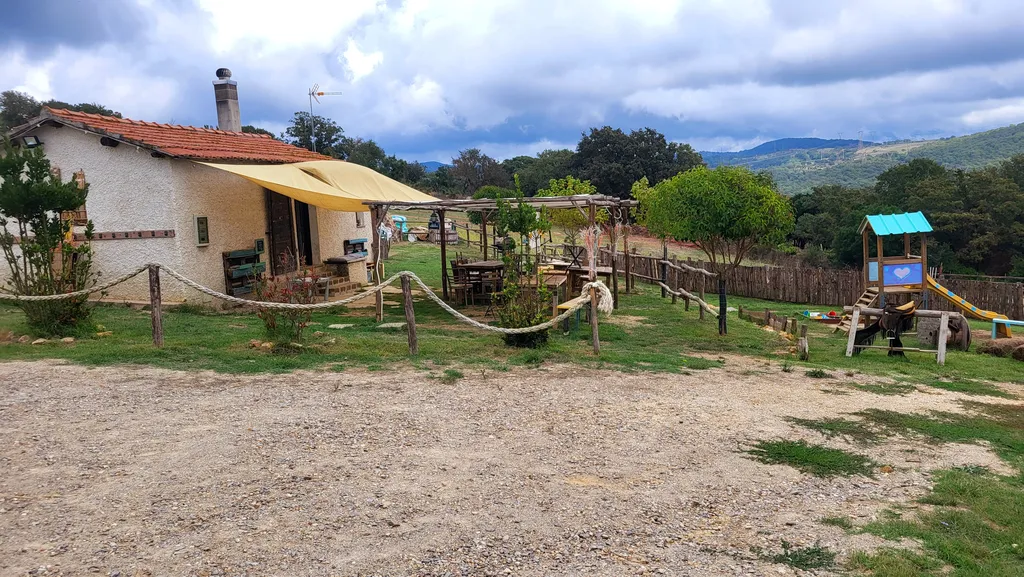 Un casale con una vela ombreggiante, davanti un parco giochi e un recinto.