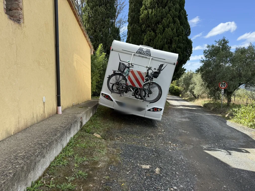 Un camper su una strada stretta fra un muro giallo e degli olivi.
