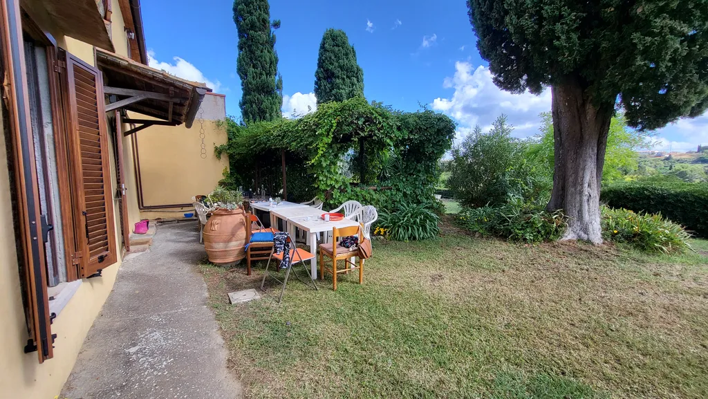 Un giardino con un grande albero e davanti una lunga tavola apparecchiata.