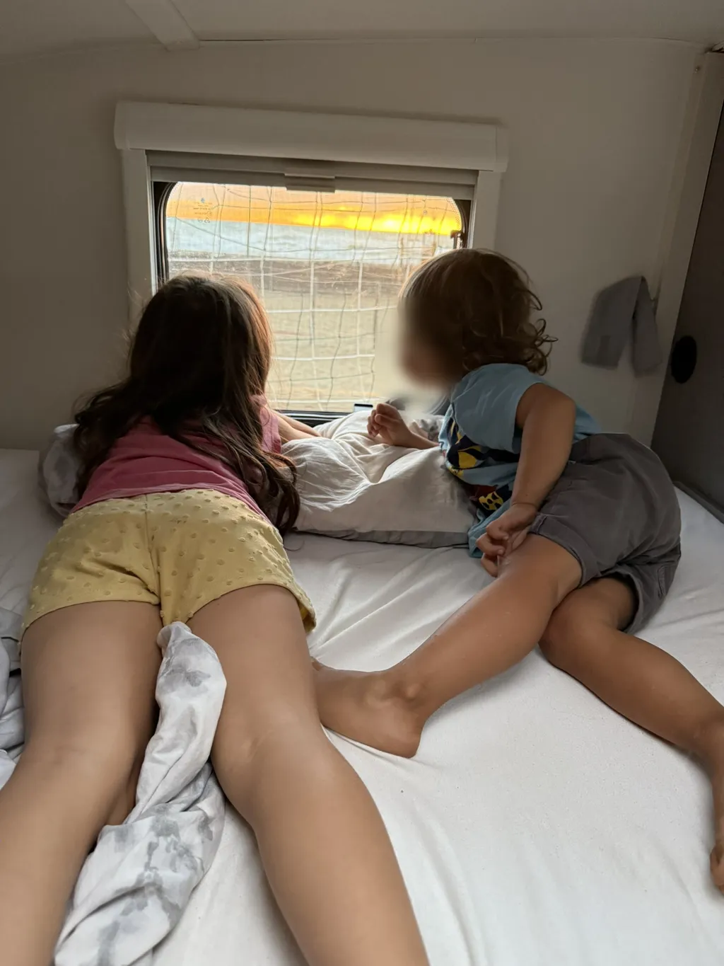 Due bambini sul letto guardano il tramonto dalla finestra del camper.