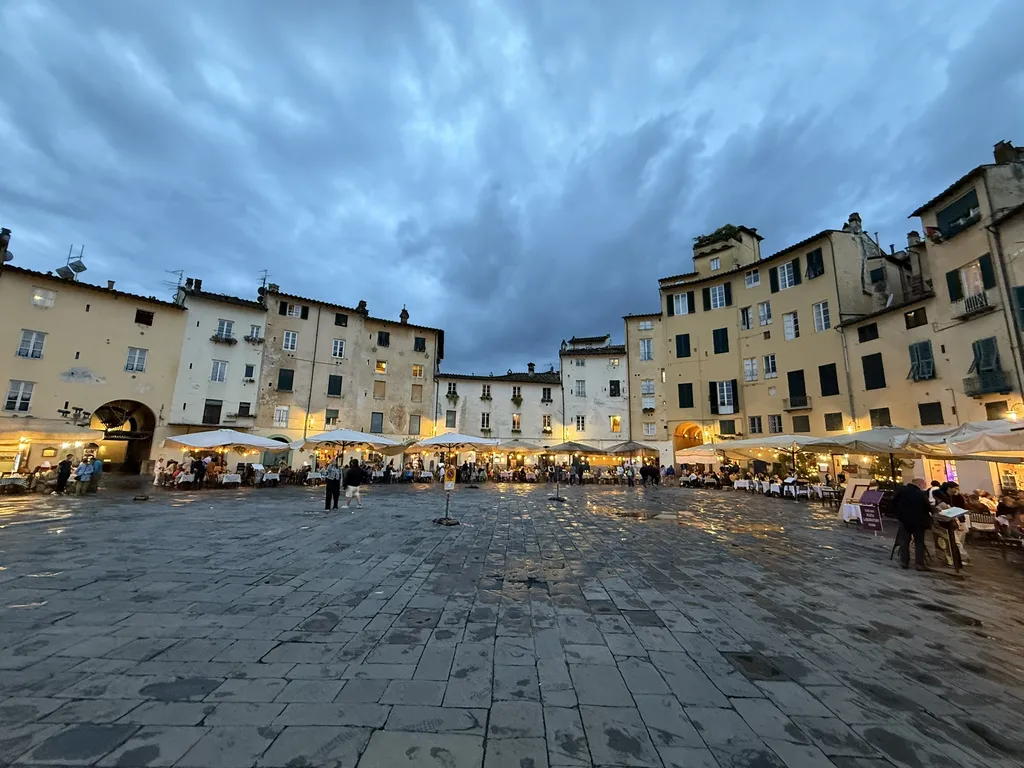 Una piazza ovale circondata da case alte, il pavimento bagnato di pioggia.