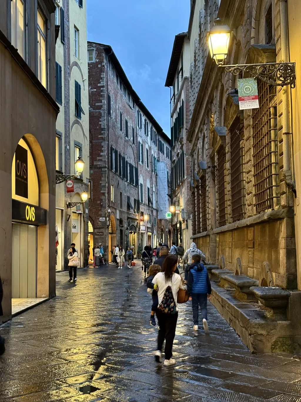 Una via dello shopping di sera, il selciato riflette le luci.