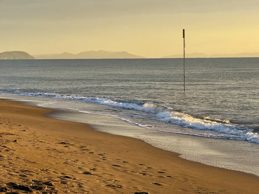 Onde basse corrono sulla sabbia, all’orizzonte si vedono monti.