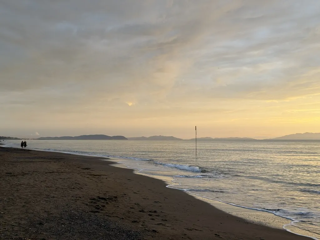 Mare e spiaggia nell’ultima luce, nell’acqua un palo sottile.