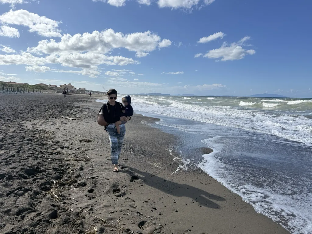 Una donna cammina lungo la spiaggia con un bambino in braccio.