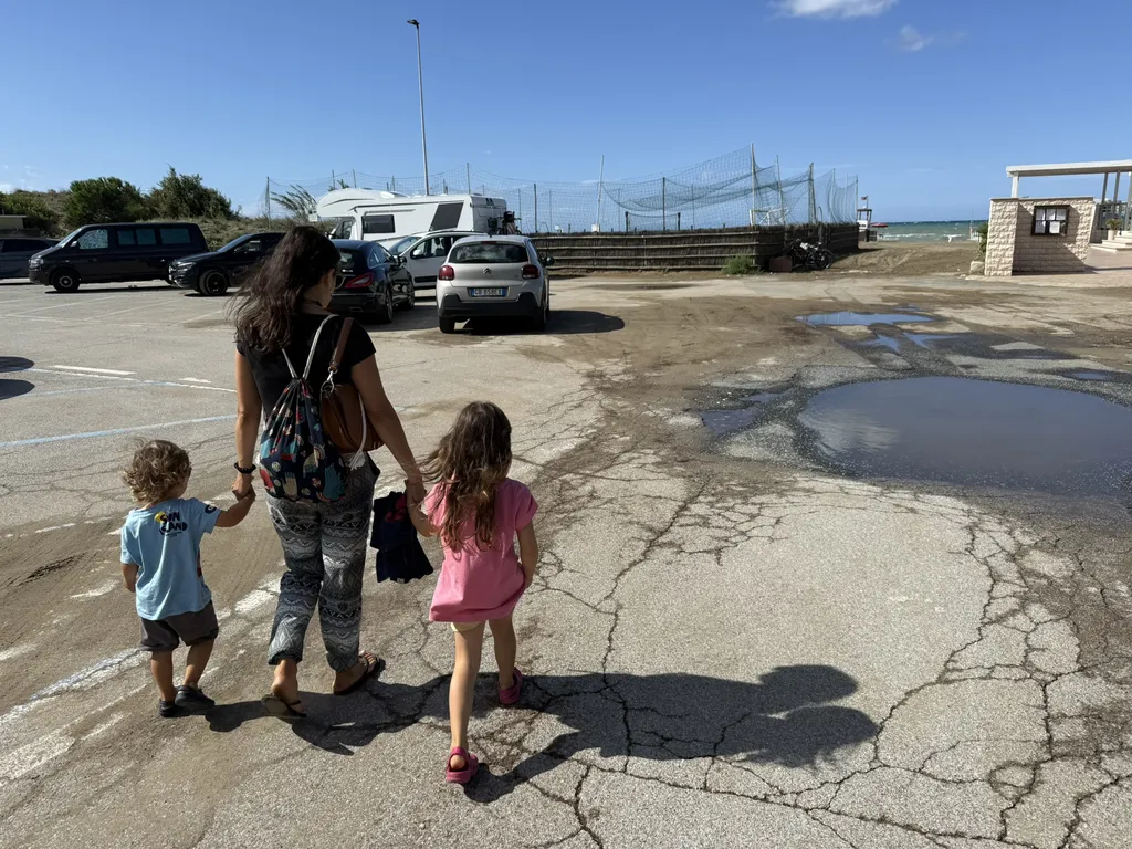 Una donna attraversa un parcheggio tenendo per mano due bambini.