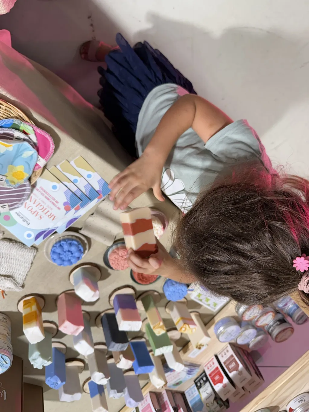 Un bambino dipinge a un tavolo pieno di colori, visto dall’alto.