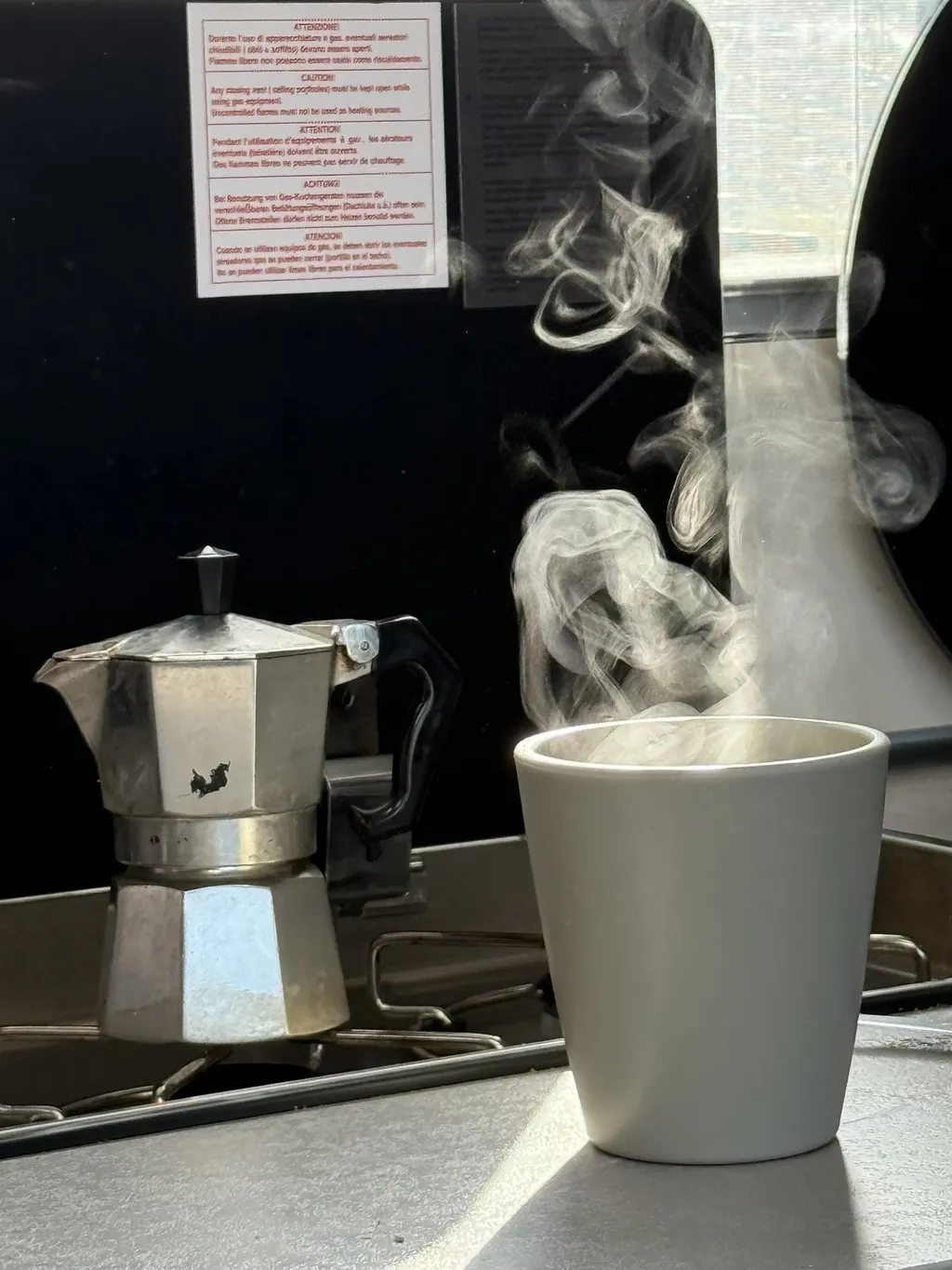 Una moka fuma sul fornello, accanto una tazza bianca.