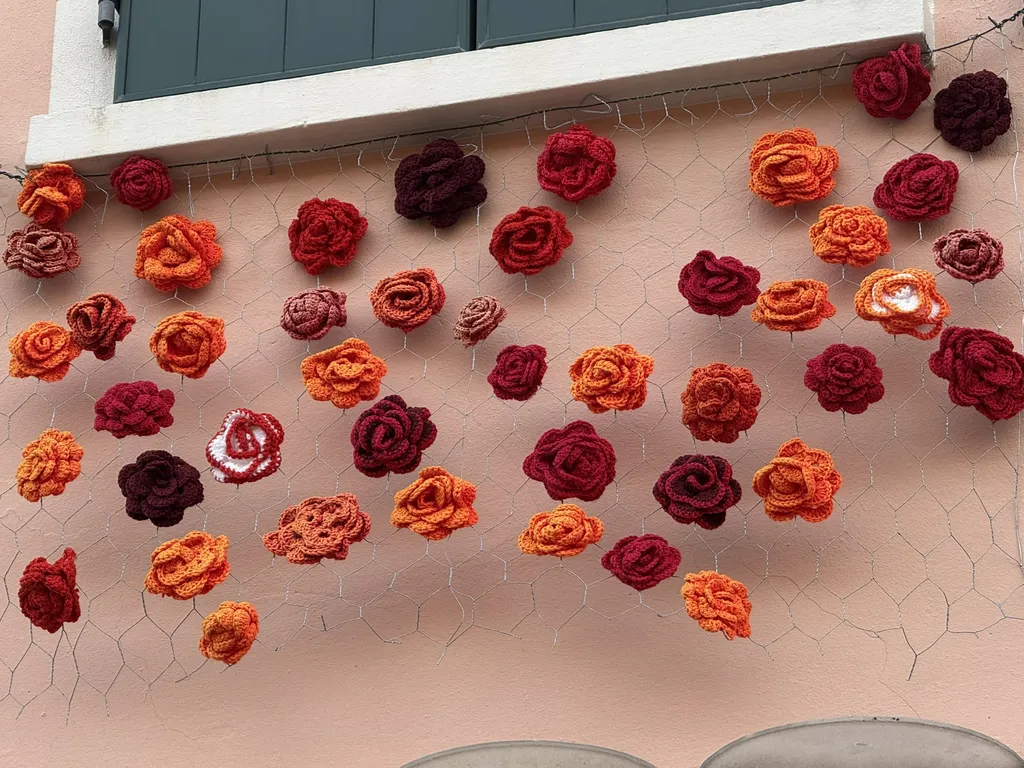 Una parete rosa piena di rose all’uncinetto rosse e arancioni.