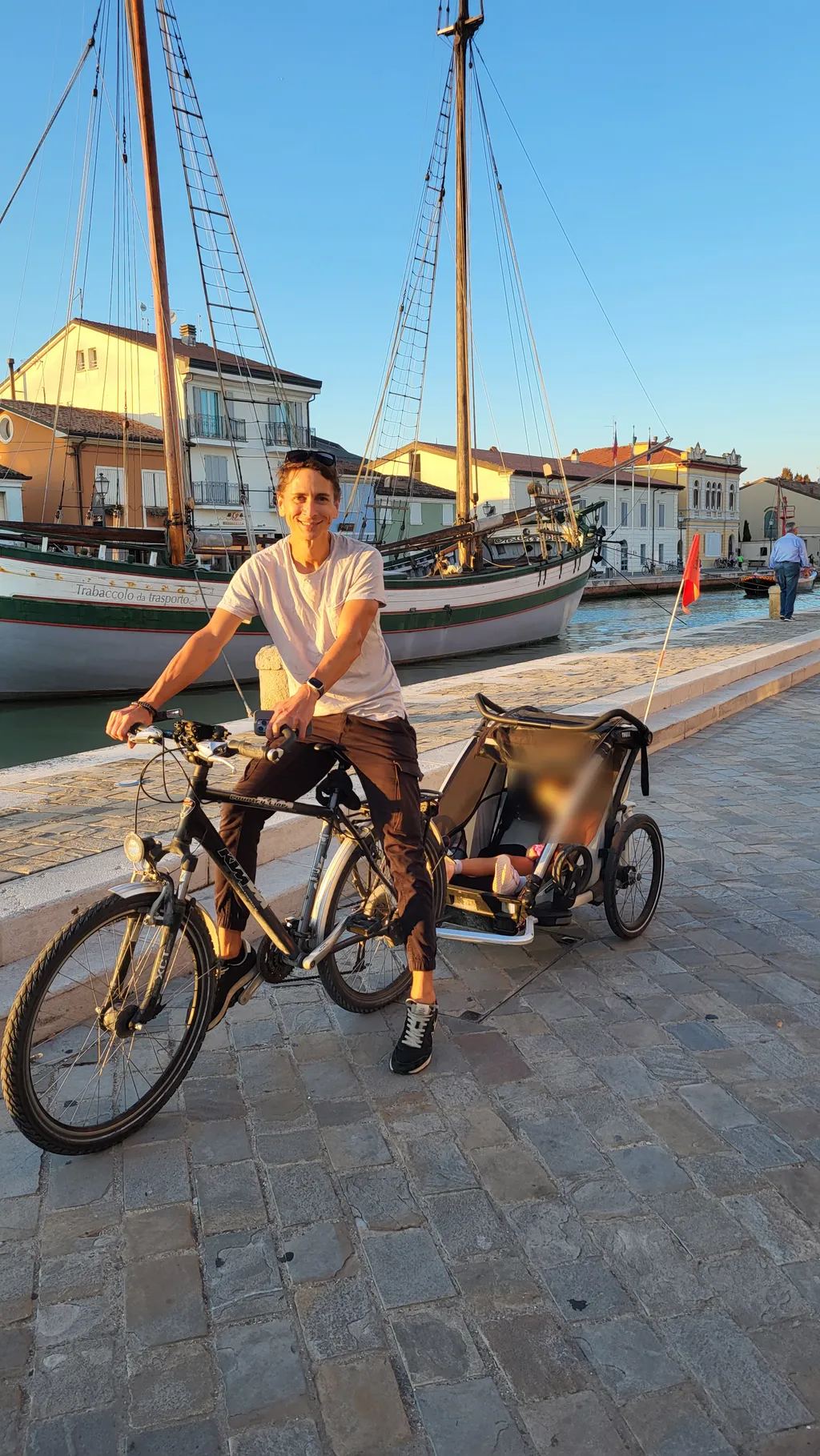 Un uomo pedala davanti a delle vecchie barche a vela.