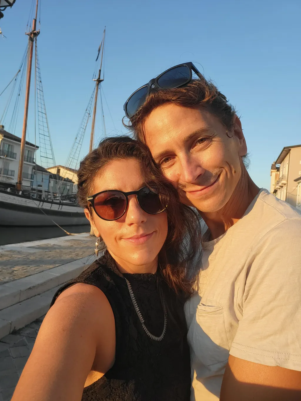 Una donna e un uomo, dietro gli alberi delle barche e il canale.