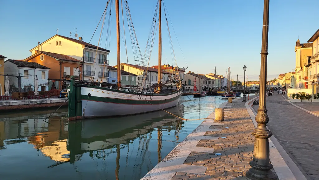 Barche a vela ormeggiate in un canale fra case colorate.